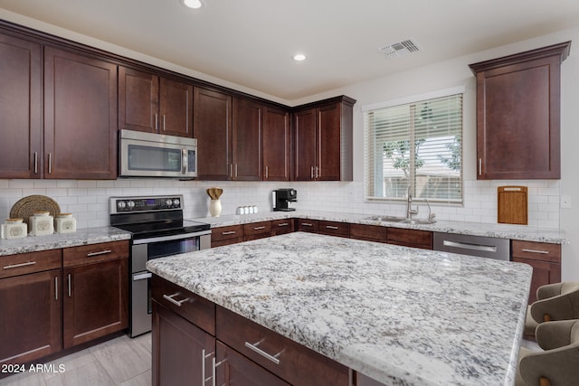 kitchen featuring sink, backsplash, stainless steel appliances, a center island, and a kitchen bar