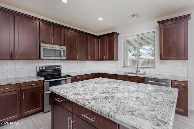 kitchen with sink, a center island, appliances with stainless steel finishes, light stone countertops, and backsplash