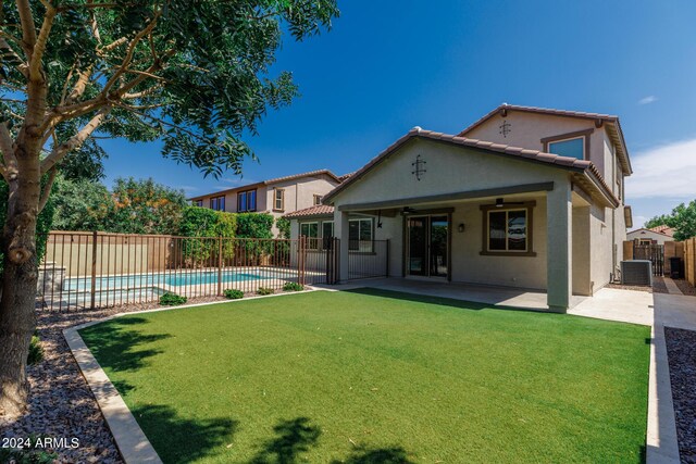 rear view of house with a lawn, a fenced in pool, ceiling fan, central AC unit, and a patio