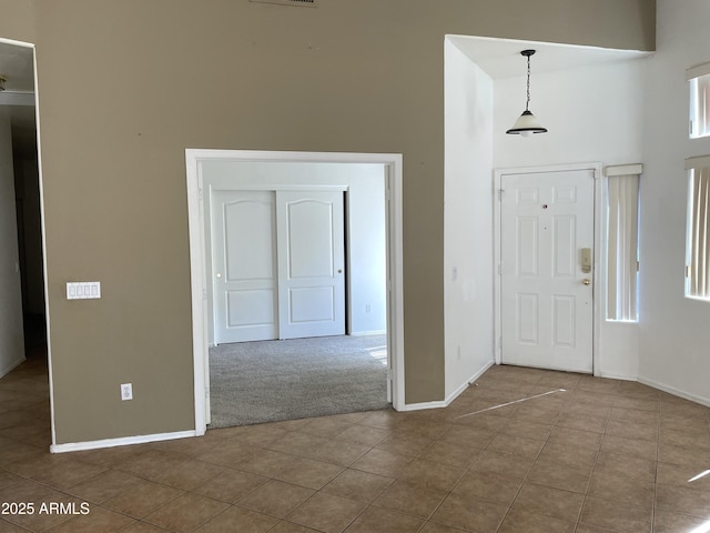 tiled entrance foyer featuring carpet floors, visible vents, a high ceiling, and baseboards