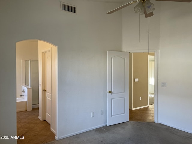 empty room featuring arched walkways, dark colored carpet, visible vents, ceiling fan, and dark tile patterned floors