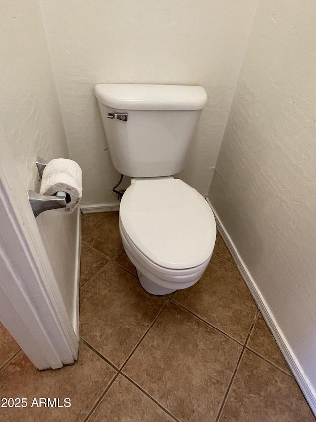 bathroom with tile patterned flooring, baseboards, a textured wall, and toilet