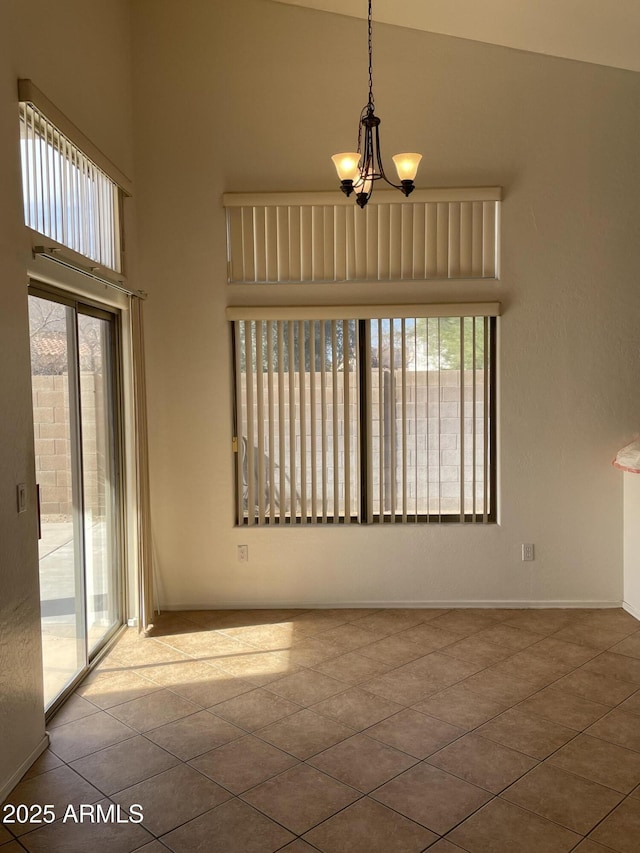 empty room with a towering ceiling, an inviting chandelier, tile patterned flooring, and baseboards