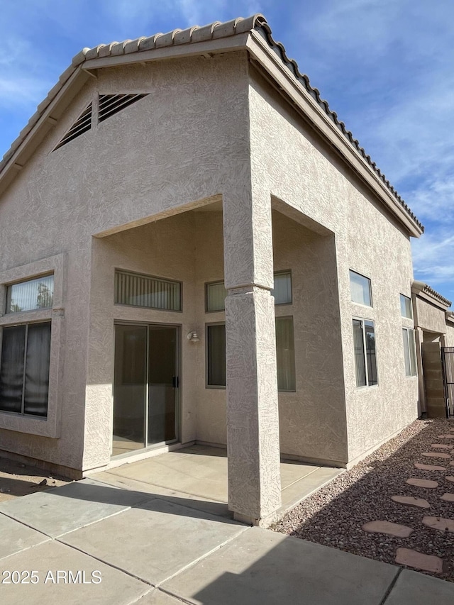 back of house featuring a tile roof, a patio area, and stucco siding