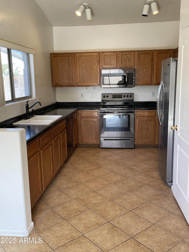 kitchen with light tile patterned floors, dark countertops, appliances with stainless steel finishes, brown cabinetry, and a sink