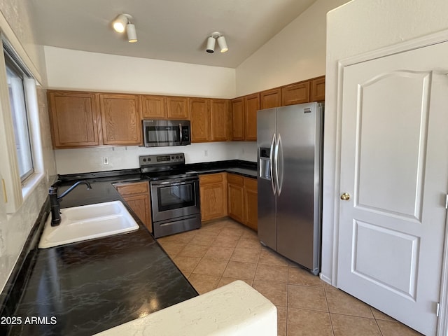 kitchen featuring light tile patterned floors, stainless steel appliances, a sink, brown cabinets, and dark countertops