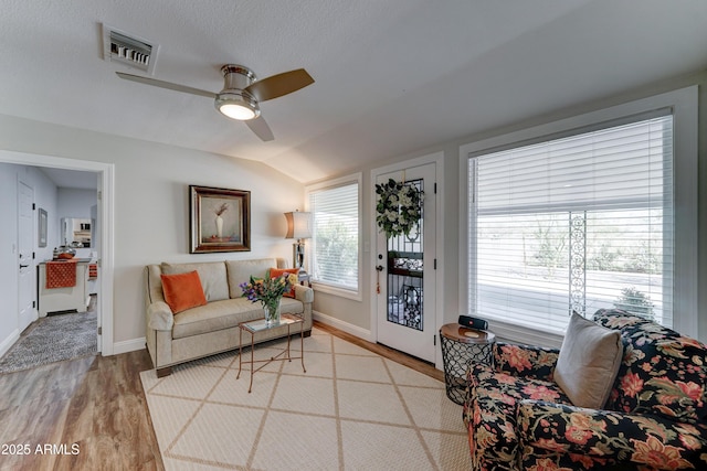 living area with visible vents, light wood-style flooring, a ceiling fan, baseboards, and lofted ceiling