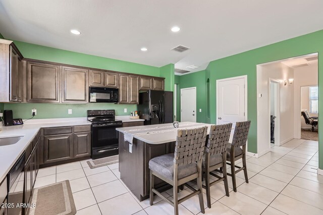 23730 W Hess Ave, Buckeye, AZ 85326 - kitchen with black appliances, a kitchen island, a kitchen bar, light tile patterned floors, and light countertops