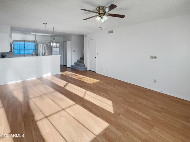 unfurnished living room with sink, ceiling fan with notable chandelier, wood-type flooring, and a textured ceiling