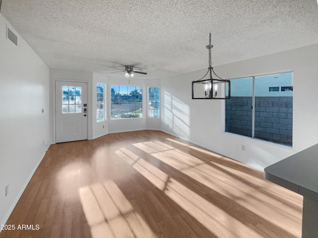 unfurnished living room with ceiling fan with notable chandelier, a textured ceiling, and light wood-type flooring