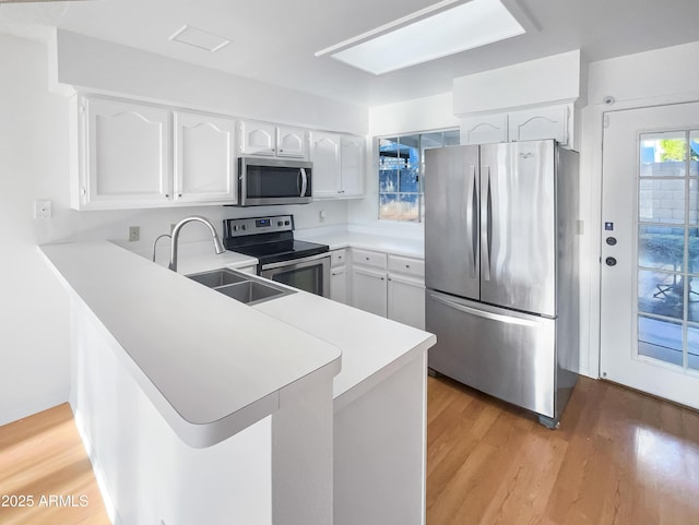 kitchen with white cabinetry, appliances with stainless steel finishes, kitchen peninsula, and light hardwood / wood-style flooring