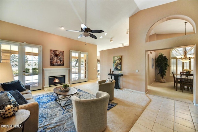 tiled living room featuring ceiling fan with notable chandelier, high vaulted ceiling, and french doors