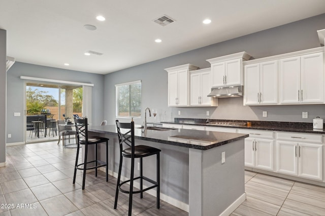 kitchen with visible vents, a kitchen island with sink, under cabinet range hood, a sink, and stainless steel gas cooktop