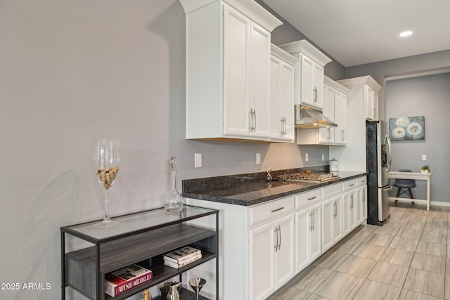 kitchen featuring under cabinet range hood, stainless steel appliances, dark stone counters, white cabinets, and baseboards