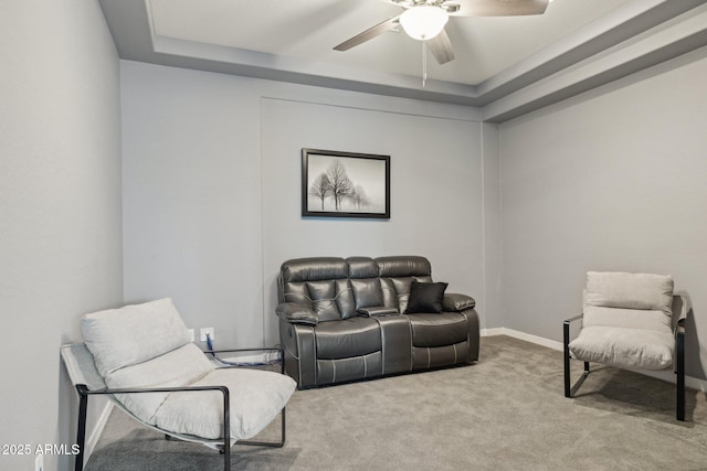 living area with a tray ceiling, carpet floors, baseboards, and ceiling fan