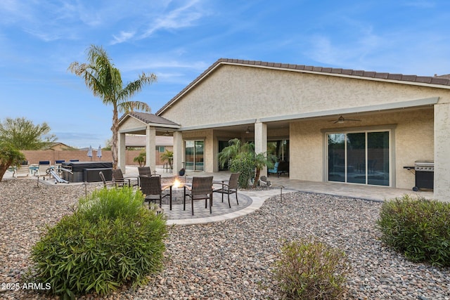 rear view of property with a fire pit, a hot tub, ceiling fan, stucco siding, and a patio area