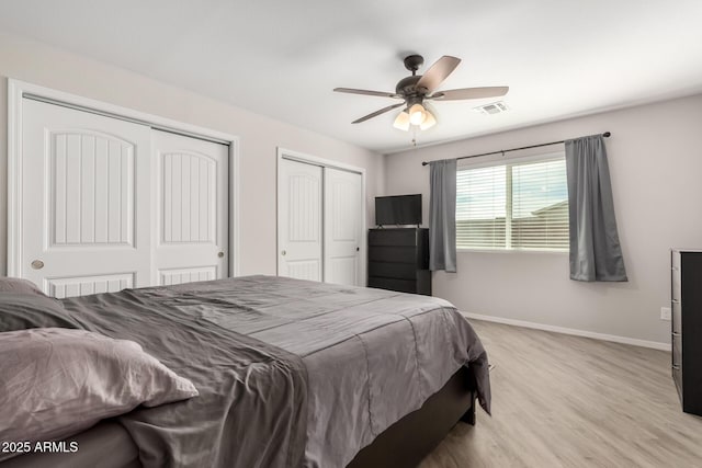 bedroom featuring baseboards, visible vents, ceiling fan, light wood-style flooring, and multiple closets