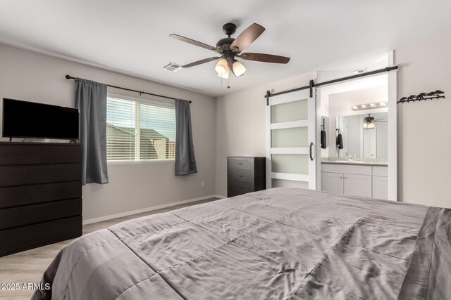 bedroom featuring visible vents, a barn door, connected bathroom, wood finished floors, and baseboards