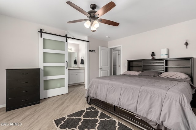 bedroom with a barn door, connected bathroom, a ceiling fan, baseboards, and light wood-style floors