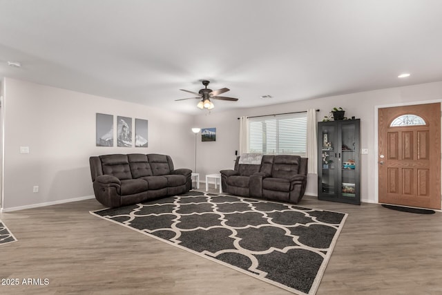 living room featuring a ceiling fan, visible vents, baseboards, and wood finished floors