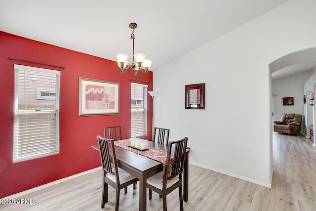 dining area featuring arched walkways, light wood finished floors, a notable chandelier, and vaulted ceiling