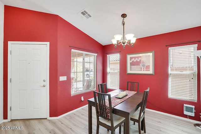 dining room with light wood-type flooring, vaulted ceiling, a chandelier, heating unit, and visible vents