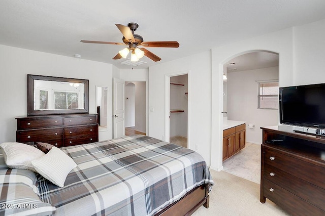 bedroom with ensuite bathroom, arched walkways, a ceiling fan, a spacious closet, and light carpet