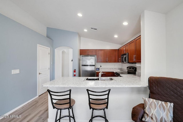 kitchen with a peninsula, vaulted ceiling, visible vents, appliances with stainless steel finishes, and a sink
