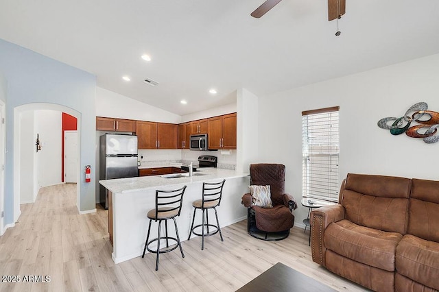 kitchen featuring a kitchen bar, a peninsula, light countertops, stainless steel appliances, and open floor plan