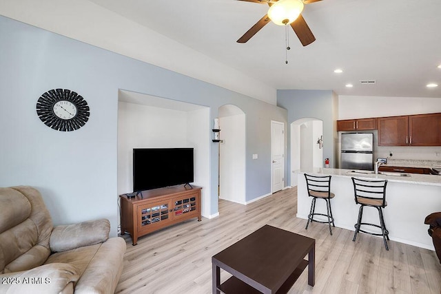 living room with arched walkways, a ceiling fan, visible vents, vaulted ceiling, and light wood finished floors