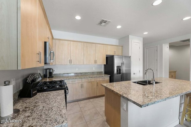 kitchen featuring visible vents, light stone counters, stainless steel appliances, light brown cabinetry, and a sink