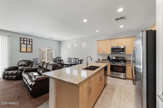 kitchen featuring stainless steel appliances, a sink, open floor plan, light brown cabinetry, and an island with sink