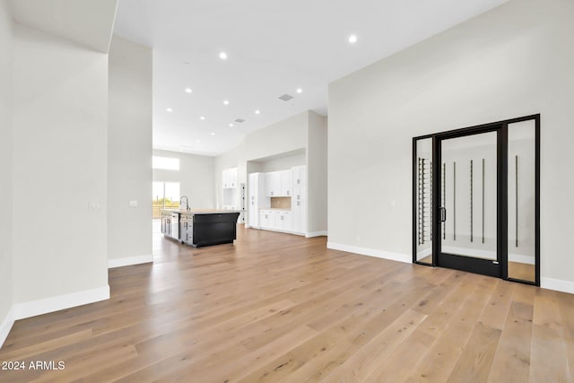 unfurnished living room with sink, light hardwood / wood-style floors, and a high ceiling