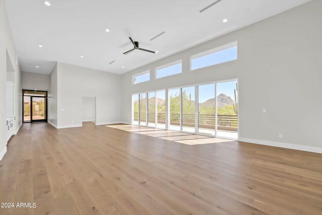 unfurnished living room featuring light wood-type flooring, a towering ceiling, ceiling fan, and a mountain view