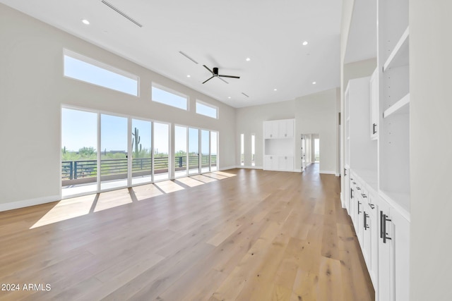 unfurnished living room with ceiling fan, a towering ceiling, light hardwood / wood-style floors, and a wealth of natural light