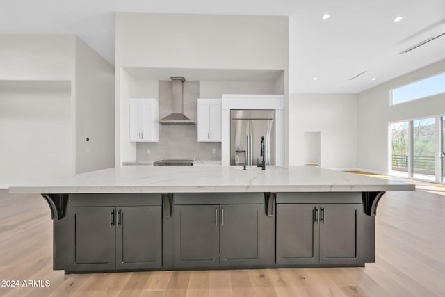 kitchen with white cabinetry, wall chimney range hood, stainless steel appliances, light stone countertops, and a spacious island