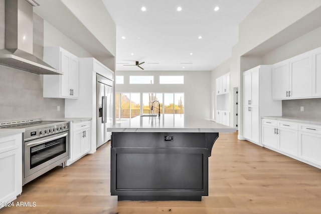 kitchen featuring white cabinets, high end appliances, wall chimney range hood, and a kitchen island