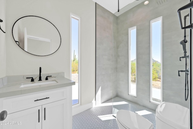 bathroom featuring vanity, tiled shower, toilet, and a healthy amount of sunlight