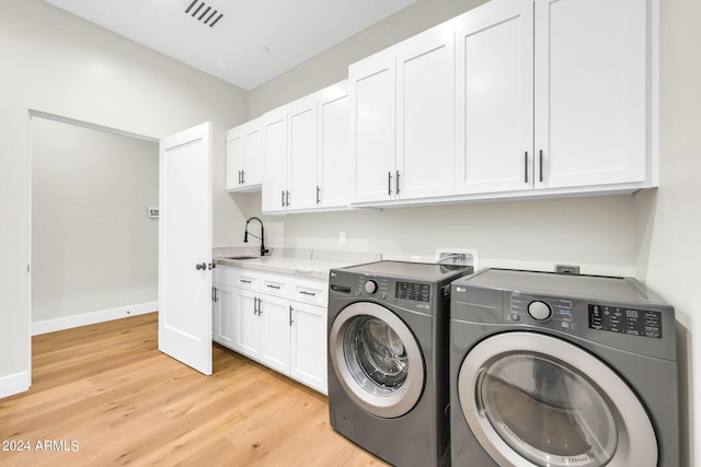 washroom with light wood-type flooring, sink, independent washer and dryer, and cabinets