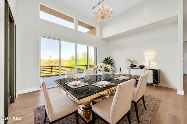 dining space with a towering ceiling, a chandelier, and light hardwood / wood-style floors