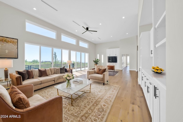 living room with a high ceiling, light hardwood / wood-style floors, and ceiling fan