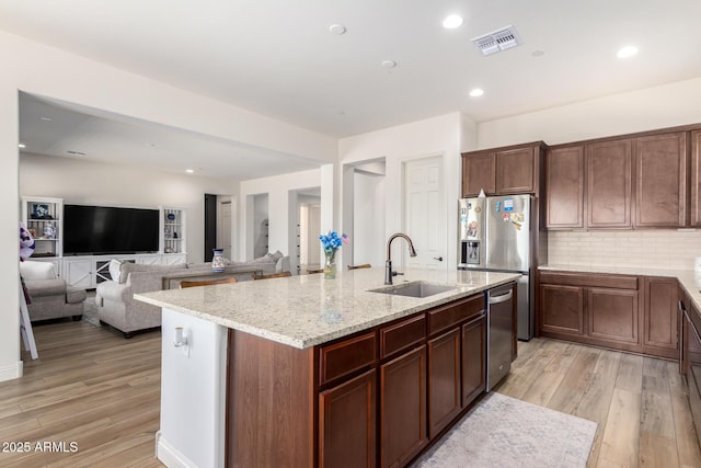 kitchen featuring visible vents, a center island with sink, light wood-type flooring, stainless steel appliances, and a sink