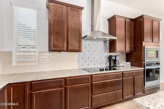 kitchen featuring light stone counters, decorative backsplash, appliances with stainless steel finishes, and wall chimney exhaust hood