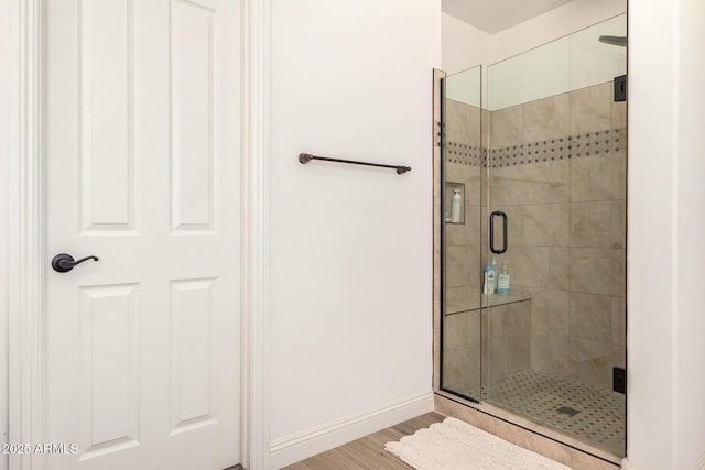 full bath with a stall shower, baseboards, and wood finished floors