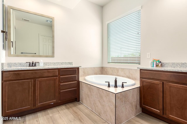 bathroom featuring visible vents, wood finished floors, a bath, and vanity