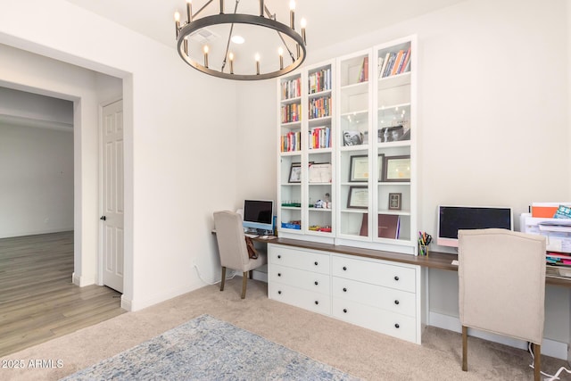 carpeted office space featuring a notable chandelier, baseboards, and built in desk