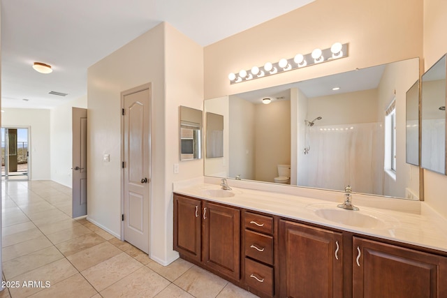 full bath featuring toilet, tile patterned flooring, double vanity, and a sink