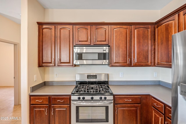 kitchen featuring light tile patterned floors, appliances with stainless steel finishes, and brown cabinets