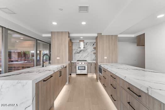 kitchen featuring range hood, light brown cabinets, a sink, high end stove, and modern cabinets