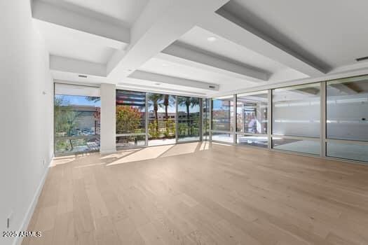 interior space featuring beam ceiling, coffered ceiling, wood finished floors, a wall of windows, and baseboards